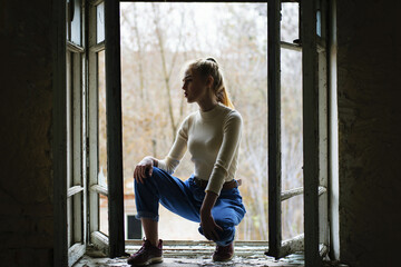 young girl sat on old window. stylish youth. old house, broken windows, beautiful young girl. emotions, lifestyle, retro, vintage. close-up. sitting on an old windowsill, open window