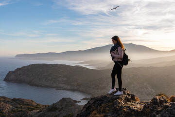 Fototapeta premium Beautiful women standing on a cliff during sunset with the sea on the background