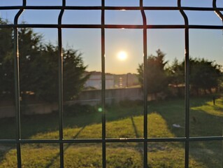 a view of the setting sun behind a wire fence. romantic