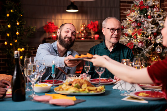 Family Having Christmas Dinner Together, Eating Traditional Food At Festive Table, Man Passing Woman Plate With Dish. People Gathering With Parents On Winter Holidays, Celebrating Xmas