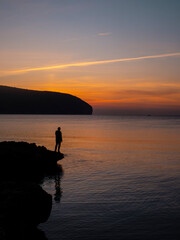 Naklejka na ściany i meble Young male watching sunrise over the sea from a rocky beach. Moraira, Calpe, Costa Brava.