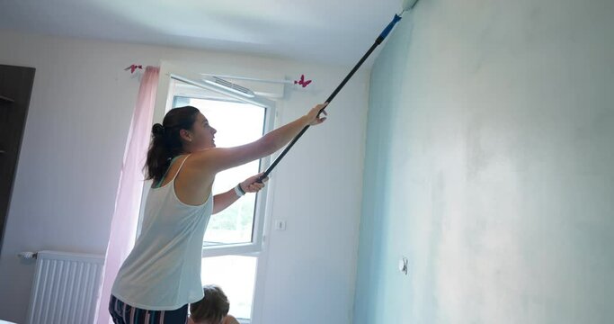 Woman painting wall with long paint roller stick at home renovation. DIY paint. Female person painter