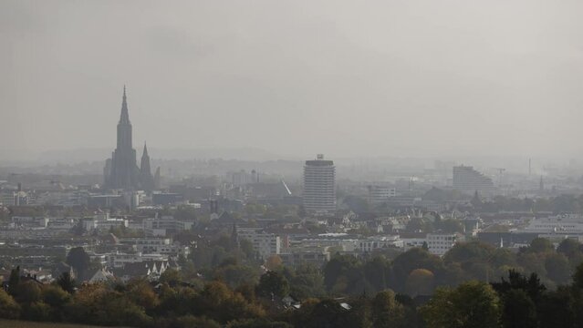 Time lapse shot of the city of Ulm with Ulm minster and colorful trees in the foreground on a foggy and misty morning in autumn