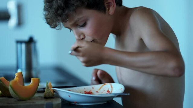 Young boy eating pasta spaghetti standing up. Candid Pre adolescent kid eats lunch quickly
