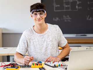 Young male technology student looking at camera with protective glasses in electronics class