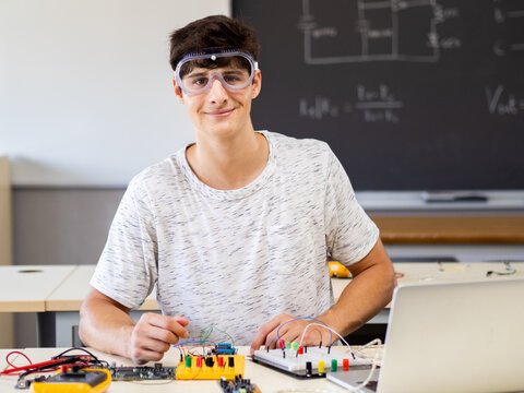 Young male technology student looking at camera with protective glasses in electronics class