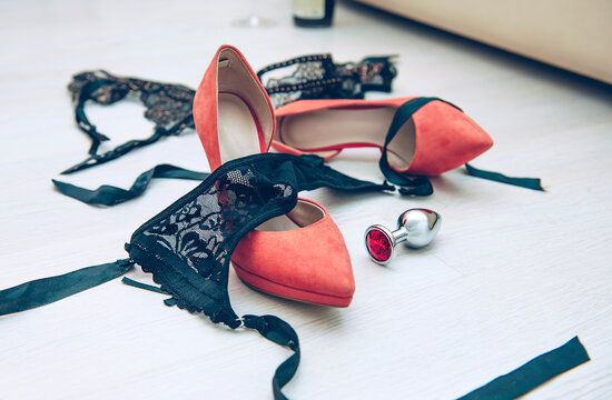Beautiful black lingerie on the floor near the bed in the room with high-heeled shoes and anal plug. Quick sex concept.