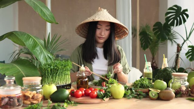 Happy young beautiful asian woman making healthy salad stirring chopped leaves indoor at exotic light studio. Healthy food at tropical home. Healthy lifestyle concept.