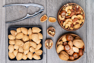 nuts in bowls and a nutcracker on a gray table. top view, Assortment of nuts - cashew, hazelnuts, almonds, walnuts, pistachio, pecans, pine nuts, peanut.