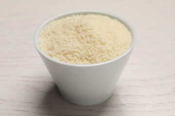 Delicious grated parmesan cheese in bowl on white wooden table