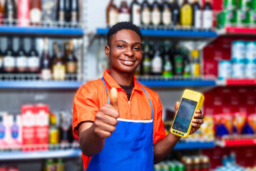 happy black male shop attendant smiling giving thumbs for approval whilst holding terminal machine - obrazy, fototapety, plakaty