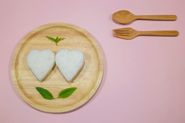 Heart shaped jasmine rice in a wooden tray on pink background.