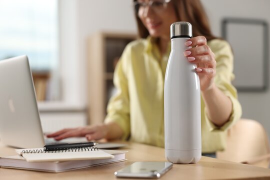 Woman holding thermos bottle at workplace, focus on container. Space for text