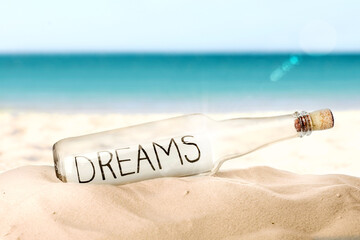 Corked glass bottle with Dreams note on sandy near sea