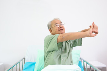 Obraz premium Happy elder Asian man sitting on the bed and making a stretch oneself in the morning. 