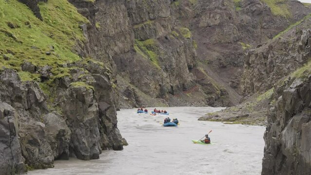 Group of boat sailing down rocky valley mountain river, distance view from back