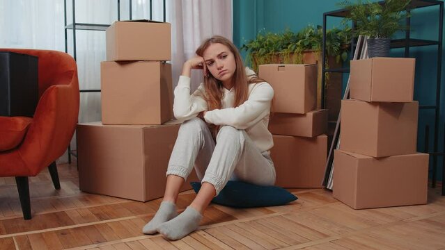 Upset depressed young woman sitting on floor near cardboard boxes with stuff. Sad girl tired of long relocation, bankruptcy, desperate due lender repossess home, bank house loan debt, divorce concept