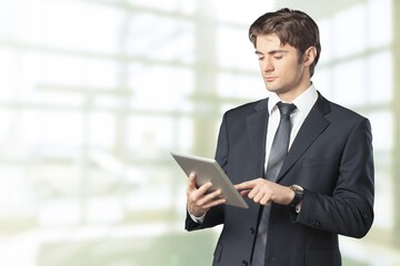 Fototapeta premium Smiling businessman with digital tablet on city background