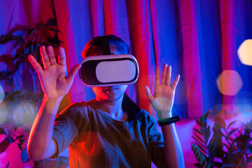 Asian woman touching air during the VR experience at home purple and blue background, female...