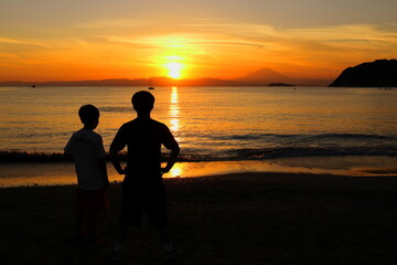 夕暮れの逗子海岸、波打ち際で夕陽を眺める兄弟の後ろ姿