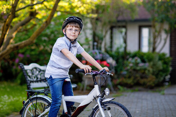 Obraz premium Happy school kid boy having fun with riding of bicycle. Active child with safety helmet making sports with bike in nature. Safety, sports, leisure with kids concept