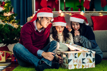 Portrait of happy family father and mother with daughter in santa hats having fun opening magic...