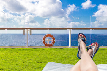 Female feet on a sunbed on a deck of cruise ship with ocean on background with blue sky and copy...