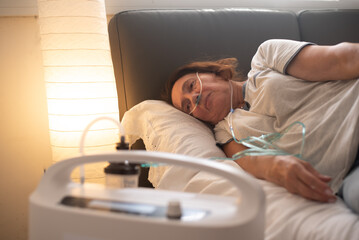 Woman lies on bed and have Oxygen breathing machine using at home. Breathing device for asthma and...