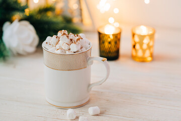 Christmas mug with hot chocolate and marshmallow with cozy garland lights and christmas tree branches on the background