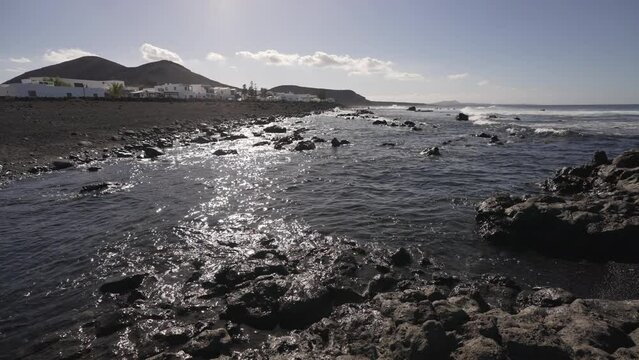 Pebble beach on Lanzarote with the village El Golfo on a sunny day