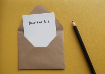 On yellow background, white card in craft envelope with handwriting DEAR PAST SELF, concept of self reflection by writing letter to person you were, advice to give about what happened then and now
