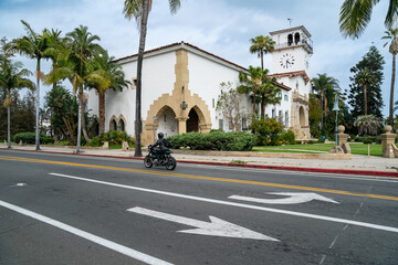 Fototapeta na wymiar California, USA - May 20, 2018: exterior of Santa Barbara country courthouse with a male motorcyclist wearing black riding motorcycle by in spring. view from the other side of road