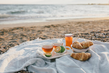 Fototapeta na wymiar Tasty summer picnic with fresh tea and croissants on the beach at sunset.