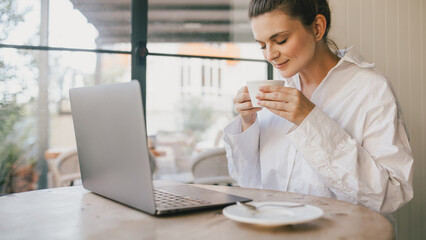 Young woman drinking coffee working online using her laptop.