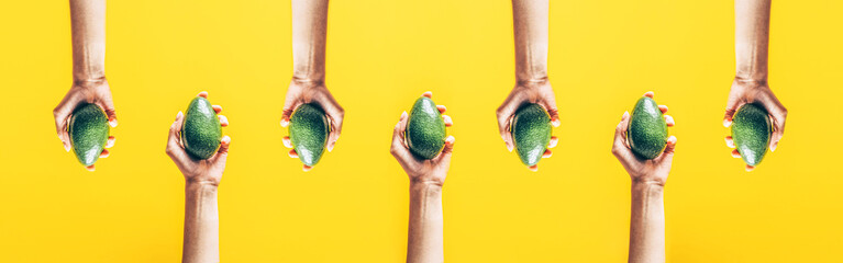 Top view of woman hands holding avocado on yellow background.