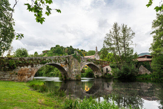 Medieval Roman bridge reflected on the water of the river Arnoia in the Galician village of Allariz on a rainy morning.