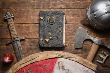 Ancient book and medieval sword, axe and shield on the table flat lay background. Knight story book...
