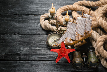 Pirate concept background. Mooring rope, compass, ship, binoculars and starfish on black wooden...
