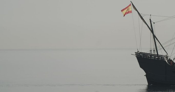 Ferdinand Magellan Nao Victoria carrack boat replica with spanish flag sails in the mediterranean at sunrise in calm sea exiting the frame in slow motion 60fps