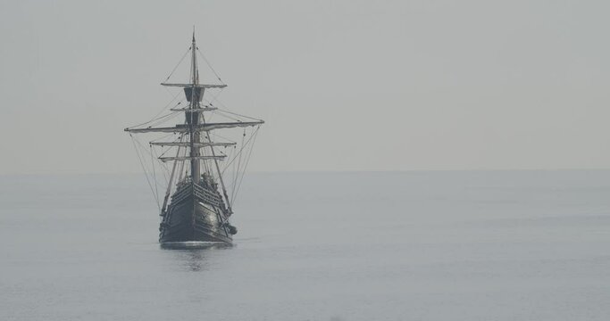 Ferdinand Magellan Nao Victoria carrack boat replica with spanish flag sails in the mediterranean at sunrise in calm sea front shot turning in slow motion 60fps