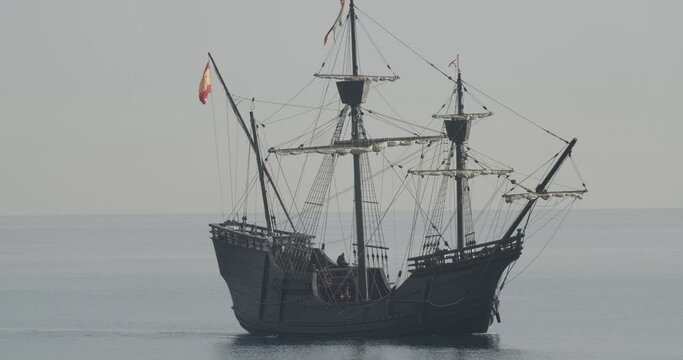 Ferdinand Magellan Nao Victoria carrack boat replica with spanish flag sails in the mediterranean at sunrise in calm sea side shot in slow motion 60fps