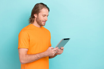 Photo of positive cute guy dressed orange t-shirt chatting apple modern gadget empty space isolated teal color background