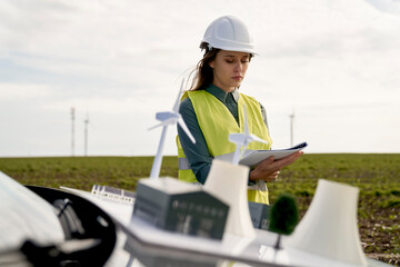 Female caucasian engineer standing on wind turbine field next to windmill field project