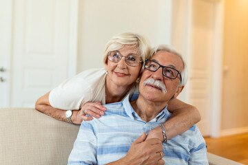 Portrait of happy senior couple embracing each other in living room at home. Elderly couple lookin each other with love and smilling
