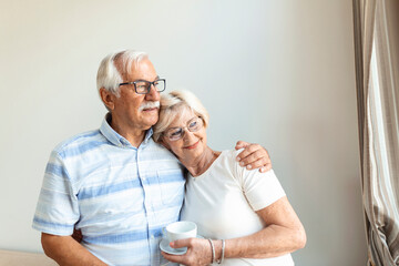 Portrait of happy senior couple embracing each other in living room at home. Elderly couple lookin each other with love and smilling