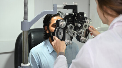 Young Indian male patient checking eye vision with phoropter eyesight measurement testing machine...