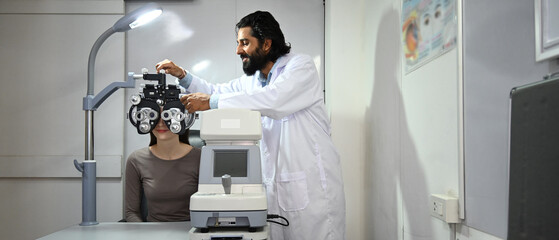 Indian ophthalmologist using medical equipment to check up eyesight of clients in clinic. Eye health check and ophthalmology concept