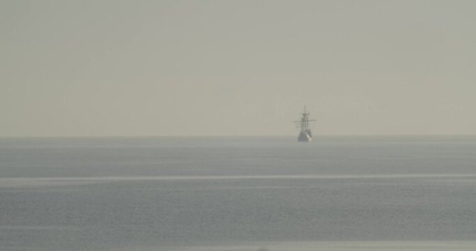 Ferdinand Magellan Nao Victoria carrack boat replica sails in the distance in the mediterranean at sunrise in calm sea in slow motion and out of focus 60fps