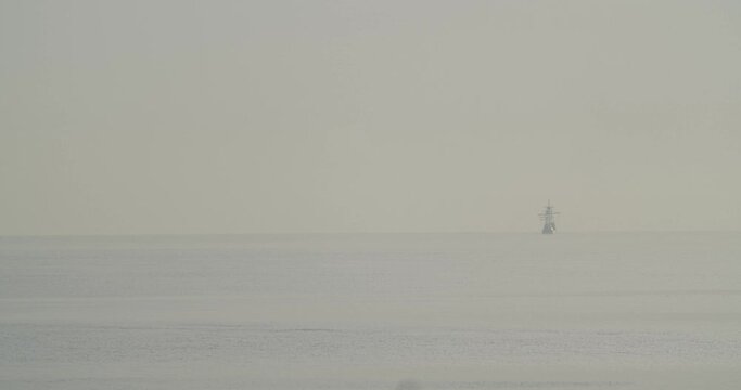 Ferdinand Magellan Nao Victoria carrack boat replica sails in the distance in the mediterranean at sunrise while a bird flies in calm sea in slow motion 60fps
