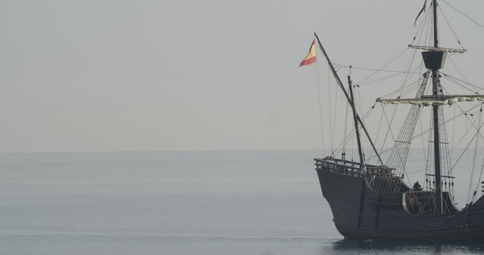 Ferdinand Magellan Nao Victoria carrack boat replica sails in the mediterranean at sunrise in calm sea side shot exiting the frame in slow motion 60fps